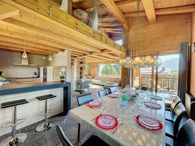 a dining room with a long table and a kitchen at Superbe chalet au calme avec jardin, garage et Wifi - FR-1-560-130 in Combloux
