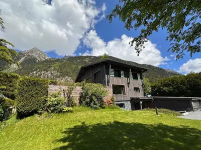 a house on a grassy hill with mountains in the background at Chalet 8 Etoiles in Chamonix-Mont-Blanc