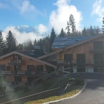 a large wooden building with mountains in the background at Appartement T2 de Standing Neuf 6-8 personnes avec Balcon et Jardinet au Pied des Pistes à Combloux in Combloux