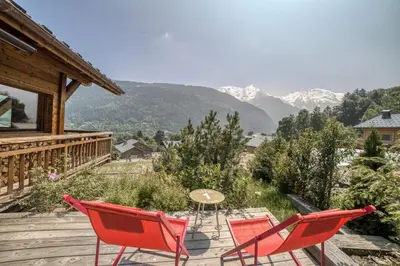 a deck with red chairs and a table and mountains at Chalet familial vue MontBlanc in Saint-Gervais-les-Bains