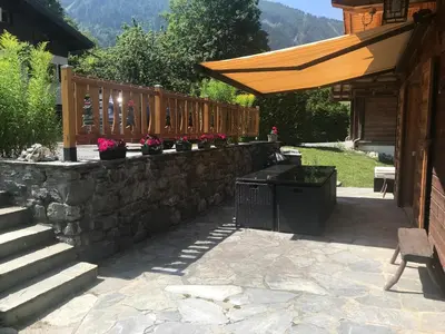 a stone retaining wall with a bench and a wooden umbrella at Superbe chalet 10 personnes 5 chambres Les Houches in Les Houches
