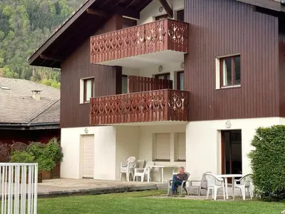 a man sitting on a chair in front of a house at Studio confortable avec parking et animaux admis - FR-1-629-139 in Samoëns