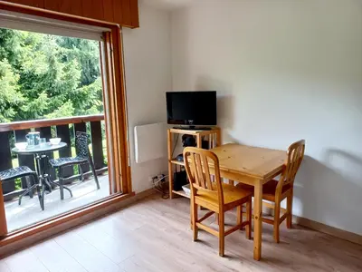 a dining room with a table and a television and a balcony at Au centre du village station de ski in Les Contamines-Montjoie