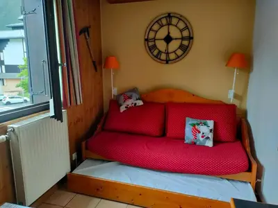 a red couch in a room with a clock on the wall at charmant appartement 2-4 personnes coeur de chamonix in Chamonix-Mont-Blanc