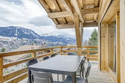 a table and chairs on a balcony with mountains at Chalet de Denis luxe alpin et emplacement ideal à Megeve in Megève