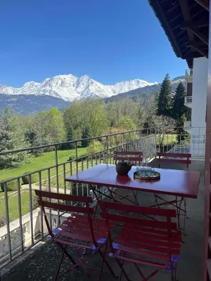 a table and chairs on a balcony with snow covered mountains at Appartement vue Mont Blanc in Combloux