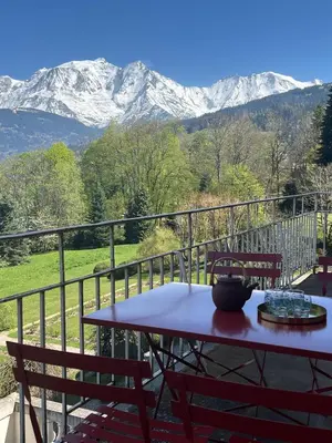 a table and chairs on a balcony with snow covered mountains at Appartement vue Mont Blanc in Combloux