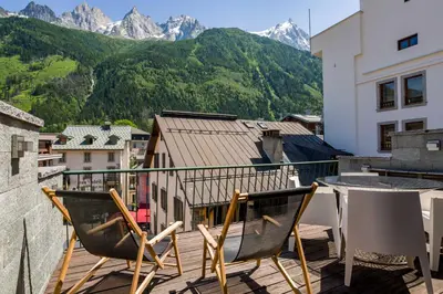 a balcony with two chairs and a table and mountains at Le Bartavel Apartment - Chamonix All Year in Chamonix-Mont-Blanc