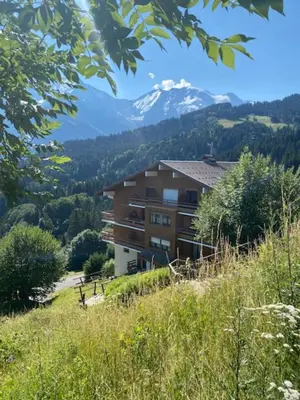 a building on a hill with mountains in the background at T2 with pool in Saint-Gervais-les-Bains in Saint-Gervais-les-Bains