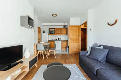 a living room with a blue couch and a kitchen at Appt MIAGE - 2 pièces cabine, terrasse & piscine in Saint-Gervais-les-Bains