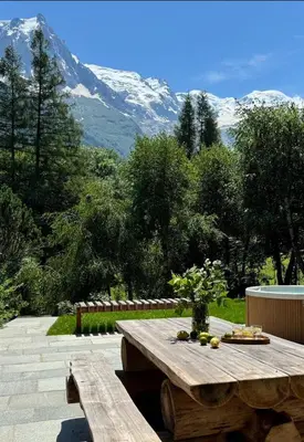 a wooden picnic table in a garden with mountains in the background at Three Bedroom Chalet Lemon Pit Chamonix in Chamonix-Mont-Blanc