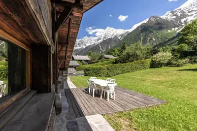 a table and chairs on a wooden porch with mountains at La Poya haut - Calme - Vues magnifiques in Les Houches