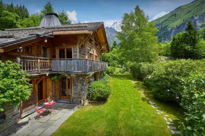 a wooden house with a green yard next to a mountain at Chalet La Chandelle - OVO Network in Bionnassay