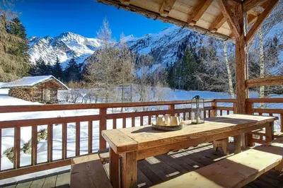a wooden table on a porch with snow covered mountains at Chalet La Chandelle - OVO Network in Bionnassay