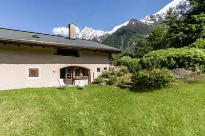 a house in a field with mountains in the background at La Poya Bas in Les Houches