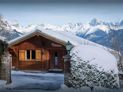 a wooden cabin in the snow with snow covered mountains at Chalet Vardache - OVO Network in Cordon