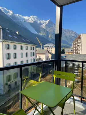 a green chair and a table on a balcony with mountains at Magnifique Studio Plein centre vue panoramique in Chamonix-Mont-Blanc