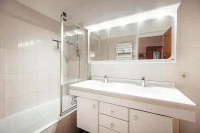 a white bathroom with a sink and a mirror at Appartement l'Olympique - Ski in & ski out in Megève
