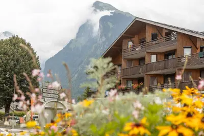 a building with a mountain in the background with flowers at Charmant appartement avec balcon et commodités modernes in Samoëns