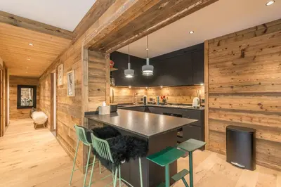 a kitchen with wooden walls and a counter with green chairs at Appartement Capra - Welkeys in Megève