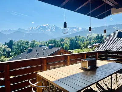 a wooden table on a balcony with a view of mountains at Chaleureux Chalet Familial - Vue époustouflante in Combloux