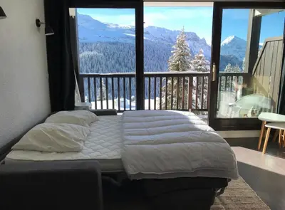 a bed in a room with a large window at Appartement à 20m des pistes, avec piscine et sauna in Arâches-la-Frasse