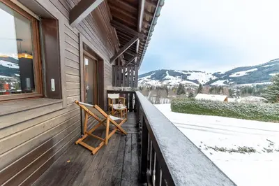 a rocking chair on a porch with a view of the mountains at Appartement à Megève skis aux pieds - La CABOCHE in Le Planellet