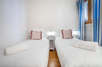 two beds in a room with white walls and blue curtains at Le Rocher - Chamonix Hypercentre - Refait à Neuf in Chamonix-Mont-Blanc