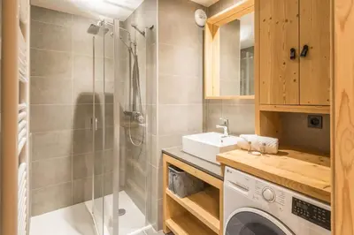 a bathroom with a shower and a sink and a washing machine at Appartement du Meu - Welkeys in Megève