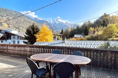 a wooden table and chairs on a deck with mountains at Appartement du Rosay - Welkeys in Saint-Gervais-les-Bains