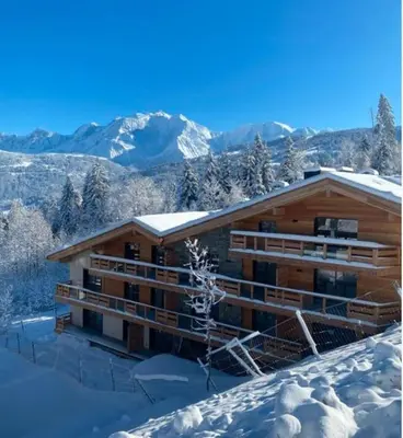a log cabin in the snow with mountains in the background at Appartement ludothèque familial neuf à Combloux in Combloux
