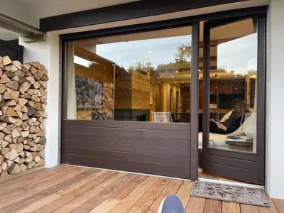 a sliding glass door of a home with a pile of wood at Appartement chaleureux à Megève - 80 m² avec jardin et cheminée. in Megève