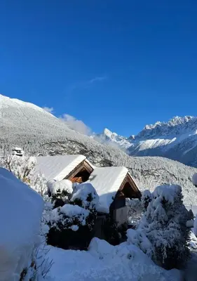 a cabin covered in snow with mountains in the background at Hameau de la Côte in Les Houches