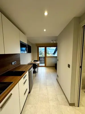 a kitchen with white cabinets and a dining room with a table at Joli petit studio neuf in Saint-Gervais-les-Bains