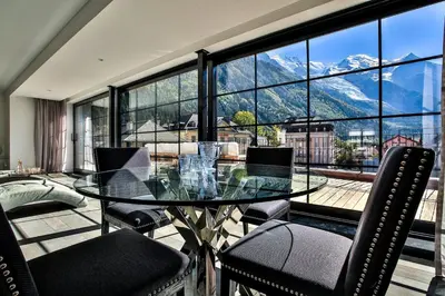 a glass table and chairs in front of a large window at Penthouse Le Lustre in Chamonix-Mont-Blanc