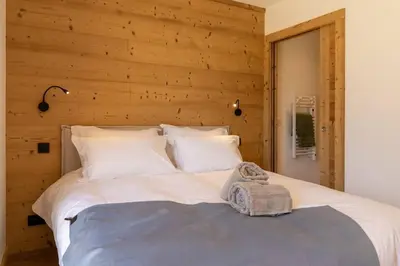 a bedroom with a white bed with a wooden wall at L'Ecrin in Plateau dʼAssy