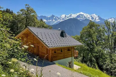 a large wooden cabin with mountains in the background at L'Ecrin in Plateau dʼAssy