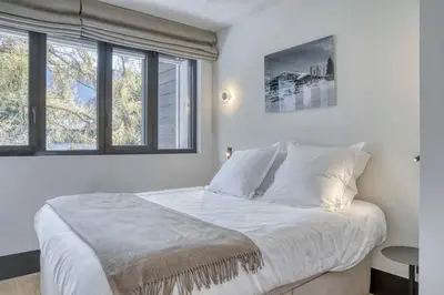 a bedroom with a bed with white sheets and windows at Appartement Orso in Megève