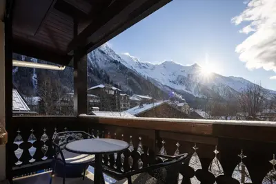 a table and chairs on a balcony with snow covered mountains at 1 bedroom apartment plus mezzanine in Chamonix-Mont-Blanc