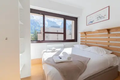 a bedroom with a bed with white sheets and a window at Appartement lumineux à Chamonix avec vue imprenable sur Mont Blanc et parking in Chamonix-Mont-Blanc