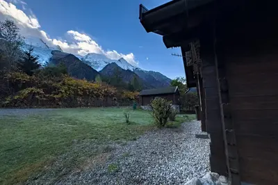 a house in a field with mountains in the background at Authentic family chalet with garden in Chamonix in Chamonix-Mont-Blanc