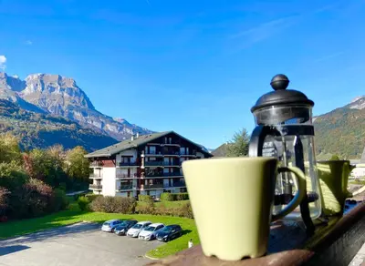 a coffee cup sitting on a fence with a building at Le coin cosy des 4 têtes - balcon - vue montagnes - proche centre & gare in Sallanches