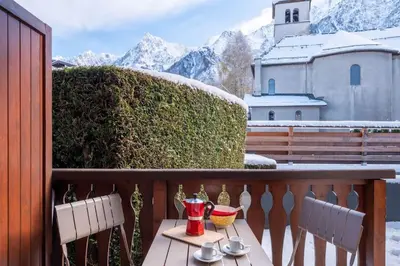 a table and chairs on a balcony with snow covered mountains at Delice - City center Les Houches & Free Parking - By Cozee Rentals in Les Houches