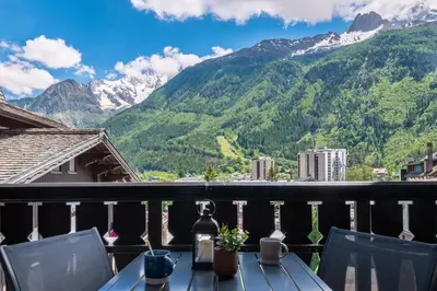 a table on a balcony with a view of mountains at Clos Savoy - New Apartment Close to City center & Free parking - By Cozee Rentals in Chamonix-Mont-Blanc