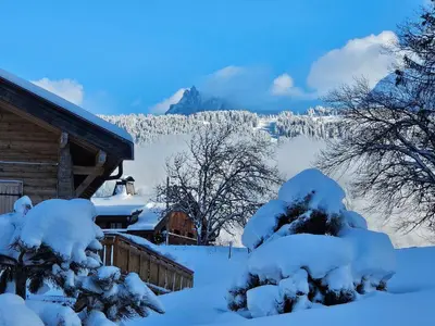 a house covered in snow with mountains in the background at Chalet la Cry à St Gervais in Saint-Gervais-les-Bains