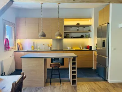 a kitchen with wooden cabinets and a island with a stool at Superbe appartement rénové 110m2 - 9 pers - vue montagne - Les Contamines in Les Contamines-Montjoie