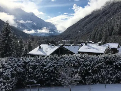 a house covered in snow with mountains in the background at Les montagnes sur le balcon in Chamonix-Mont-Blanc