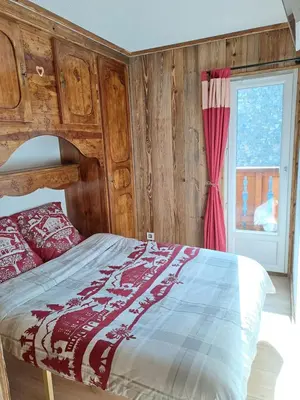 a bedroom with a bed with a wooden headboard and a window at Appartement équipé centre Carroz et garage in Arâches-la-Frasse