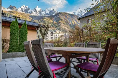 a wooden table and chairs on a patio with mountains at Alpine Garden - Truly hidden gem with sunny garden in Chamonix town center in Chamonix-Mont-Blanc