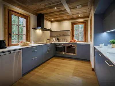 a large kitchen with blue cabinets and wooden ceilings at Chalet Les Pellys - OVO Network in Samoëns